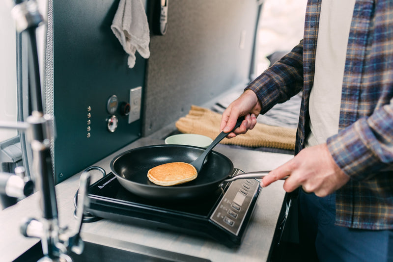 Making breakfast in an RV rental: a person flips a pancake on a portable stove in a cozy camper kitchen. — photo 19