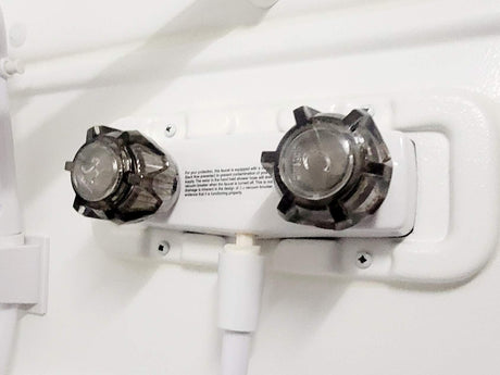 This RV rental's white shower faucet features dual clear handles and a hose connection. Note visible text on backflow prevention.