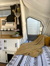 Cozy RV rental interior showcasing a bed, textured blanket, and decorated storage space. Perfect for your next adventure.