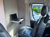 Mobile office setup in an RV rental: laptop on a fold-down desk, with power outlets and plush seating.