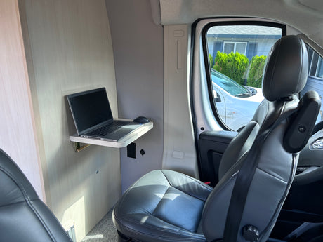 Mobile office setup in an RV rental: laptop on a fold-down desk, with power outlets and plush seating.