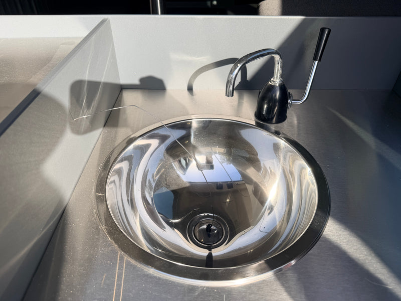 Shiny stainless steel sink & faucet in an rv rental's grey kitchenette. Sunlight highlights the metal & wall textures, casting shadows. — photo 9