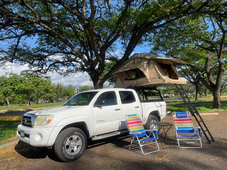 White Tacoma truck with rooftop tent & chairs, offering a unique RV rental camping experience under trees.