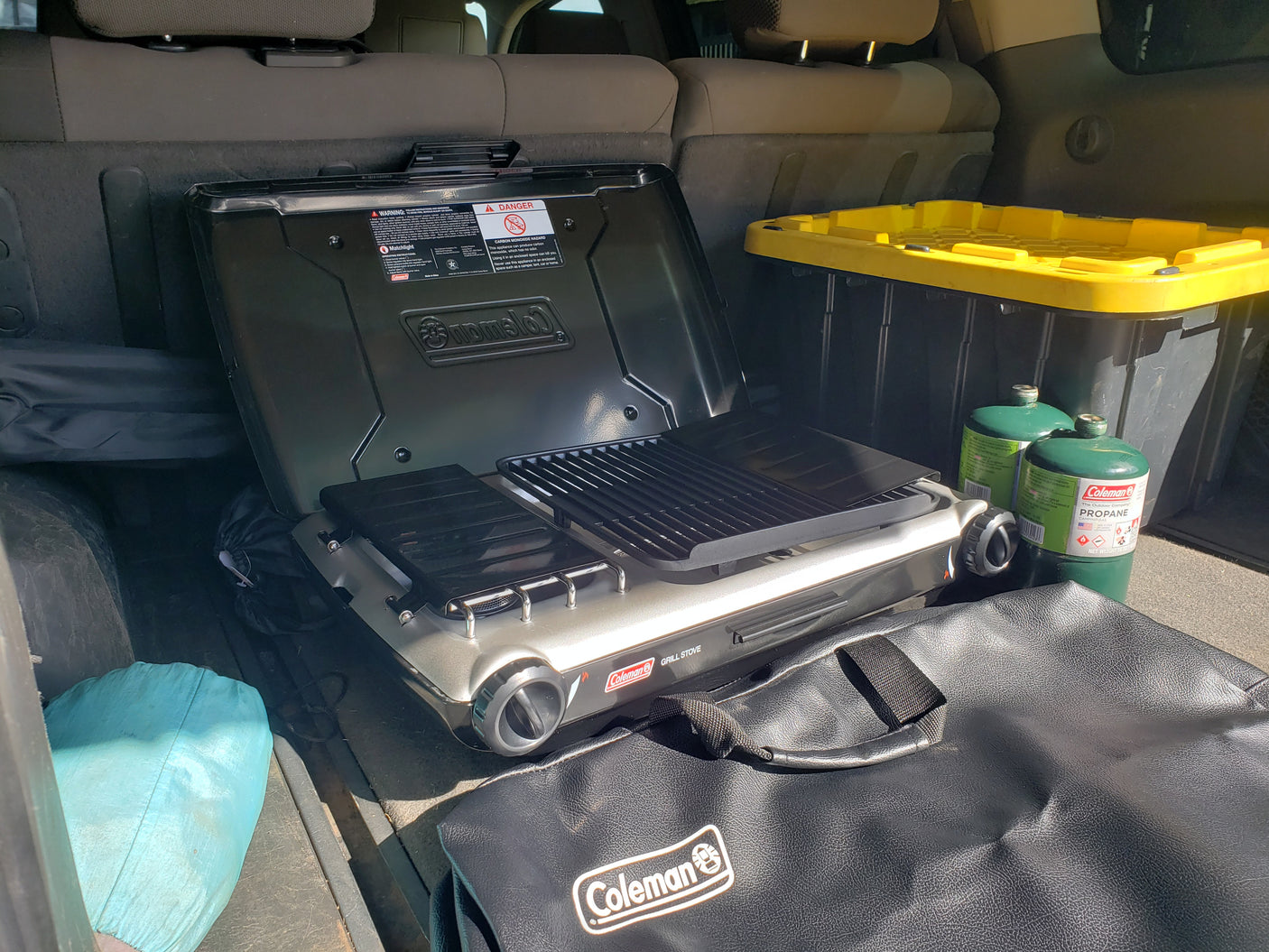Coleman camping grill, propane tanks, and gear packed for an RV rental adventure, ready for outdoor cooking.