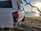 White Toyota Tacoma with camper shell, parked on a sandy beach. An RV rental for rugged outdoor adventures awaits!