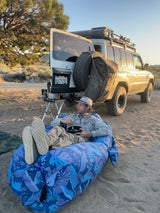 Man enjoys a meal from an inflatable chair next to his overlanding SUV. An ideal RV rental for desert camping adventures.