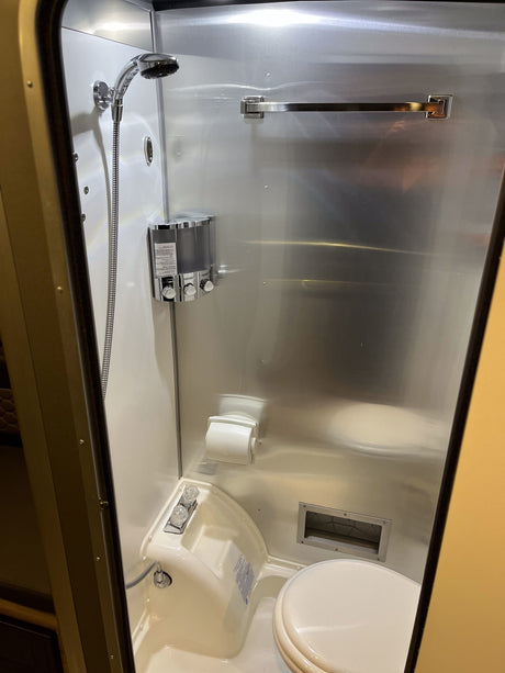 Inside an RV rental: a compact bathroom featuring a shower, toilet, and modern dispensers.