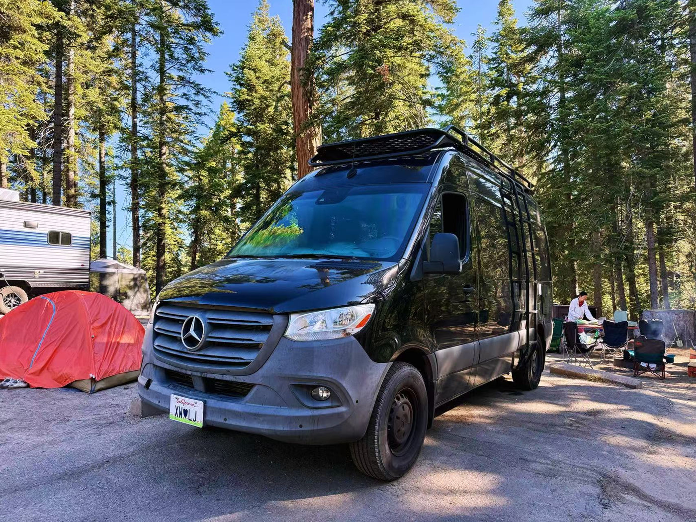  is ready for camping at dusk.|Sleek black RV rental (Mercedes Sprinter) reflecting tall trees — photo 5