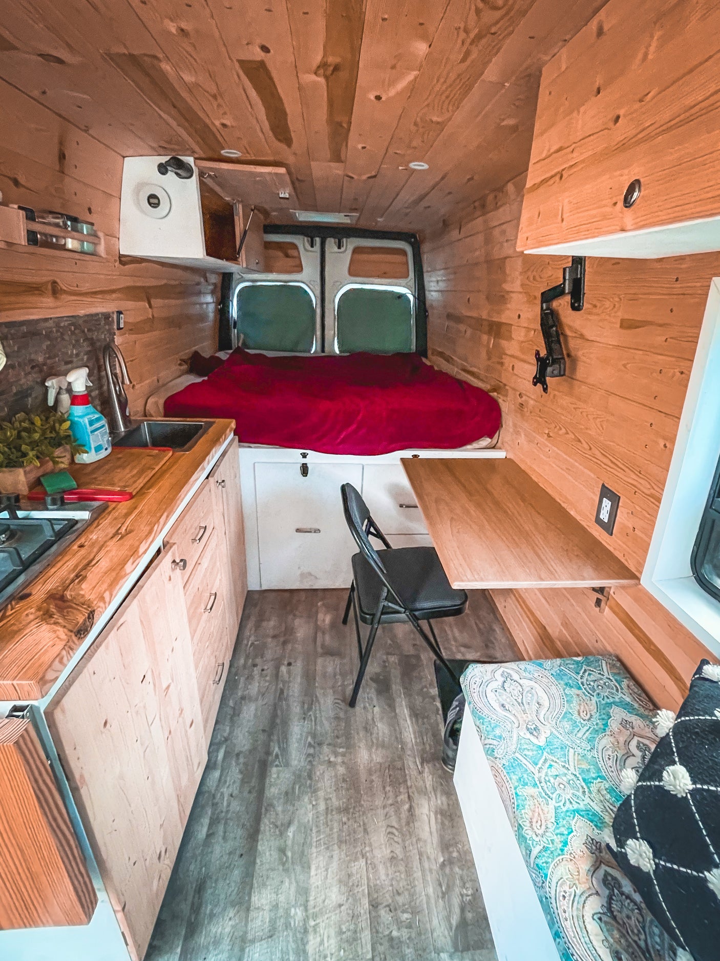 **rv rental:** Inside a rustic wood-paneled van: kitchen, bed, workstation, and seating. Your compact home on wheels awaits!