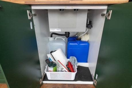 Inside an RV rental cabinet: Compact sink system with water tanks and essential cleaning supply storage.