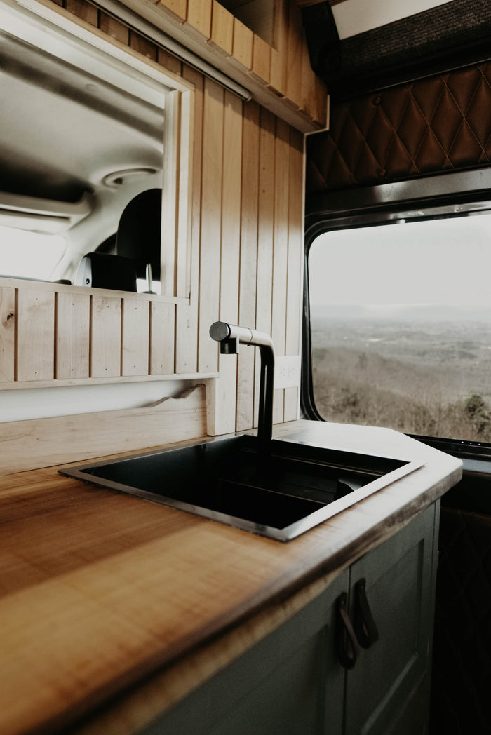 and a scenic window overlooking rolling hills.|RV rental's functional kitchen: a black true Induction cooktop on a light wood counter
