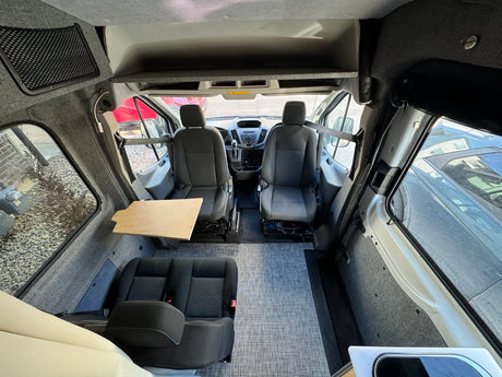 RV rental: Interior view of a spacious custom camper van, featuring front seats, a rear bench, and a wooden side table.