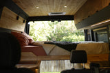 Cozy RV rental camper van interior: wood paneling, comfortable bed, bright lights, and nature views.