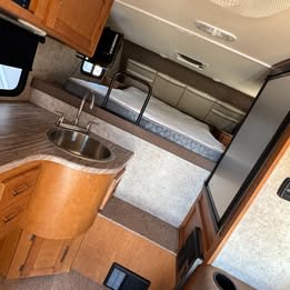  with stairs extended for easy access under a carport.|Interior view of an RV rental: a compact kitchenette with sink and a raised bed area. Perfect for camper adventures.|RV rental interior featuring a Dometic refrigerator