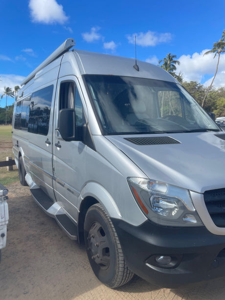 Silver Mercedes-Benz Sprinter camper van for rv rental, parked under a blue sky with palm trees.