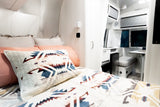 Inside a stylish RV rental: cozy bedroom with geometric bedding, sleek walls, and functional dinette area.