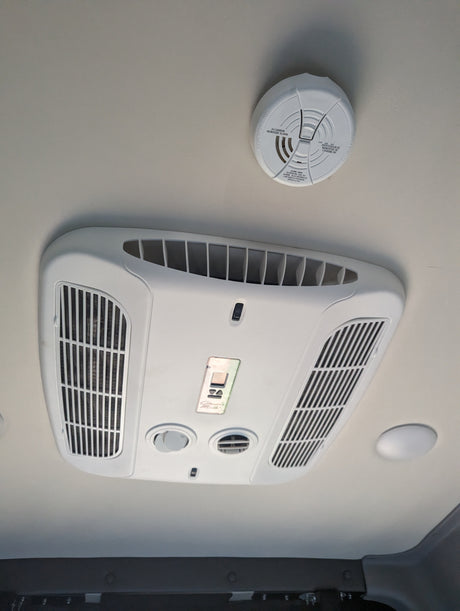 RV rental ceiling: an air conditioning unit, carbon monoxide alarm, and lights for safety and comfort inside.