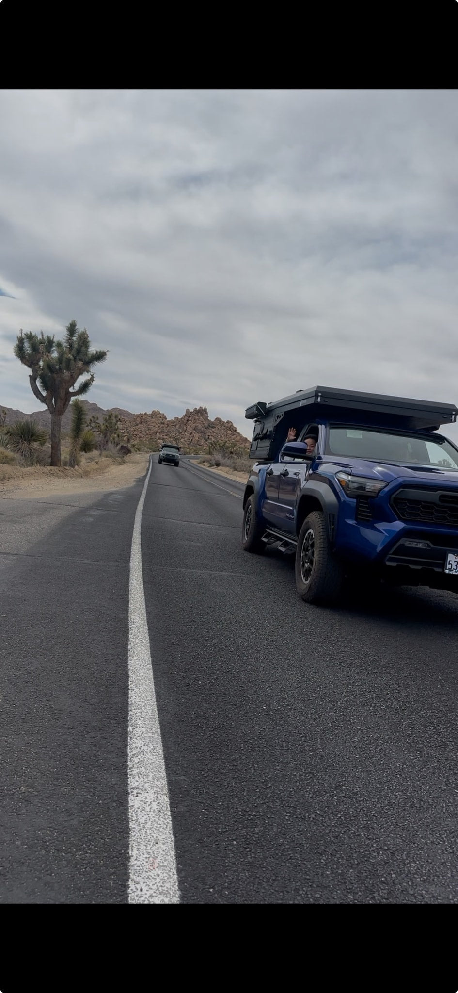 A blue truck with a rooftop camper drives on a desert road