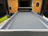 RV rental: Camper van's extended pull-out cargo tray with a textured mat, flanked by wood panels containing a gauge and water connections.