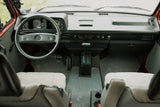 Front view of a vintage VW RV rental interior: dashboard, steering wheel, and gear shift visible. Ready for adventure.