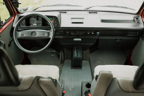 Front view of a vintage VW RV rental interior: dashboard, steering wheel, and gear shift visible. Ready for adventure.