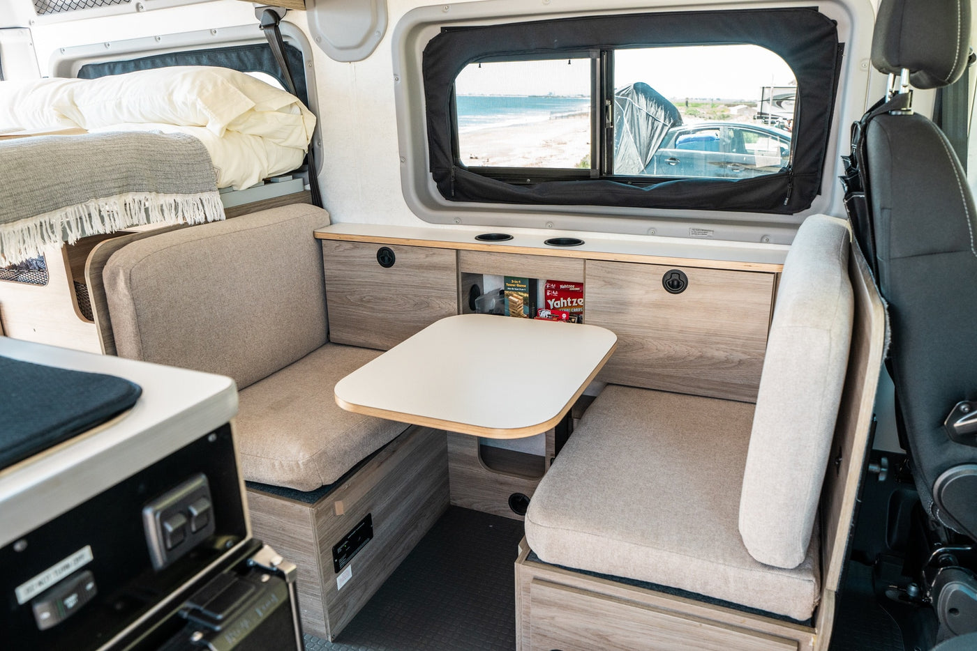 Inside this RV rental: a comfy dinette with table & seating, a cozy overhead bed, and a window view of the beach. Ideal for travel. — photo 13