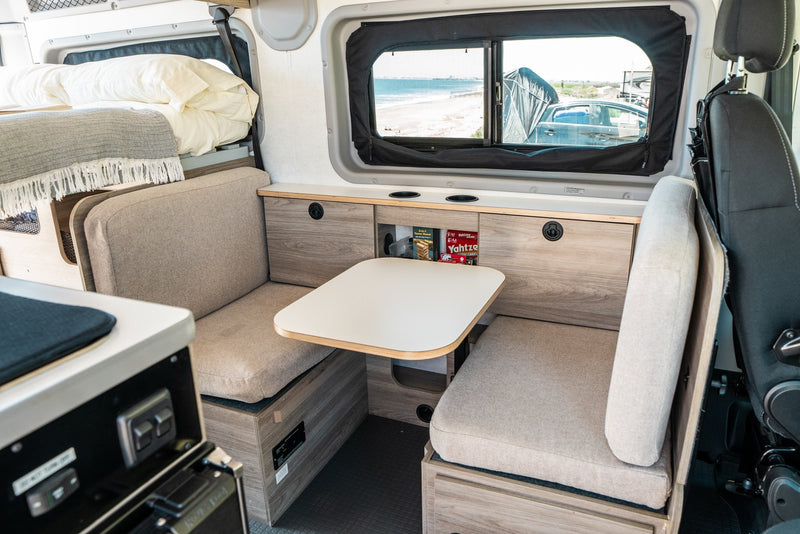 Inside this RV rental: a comfy dinette with table & seating, a cozy overhead bed, and a window view of the beach. Ideal for travel. — photo 13