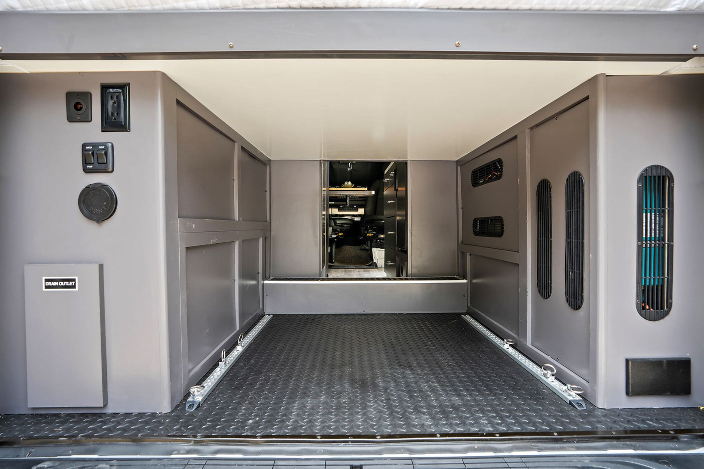 RV rental's rear utility area: power outlets, water/light controls, drain, vents, & floor tie-downs for secure cargo.