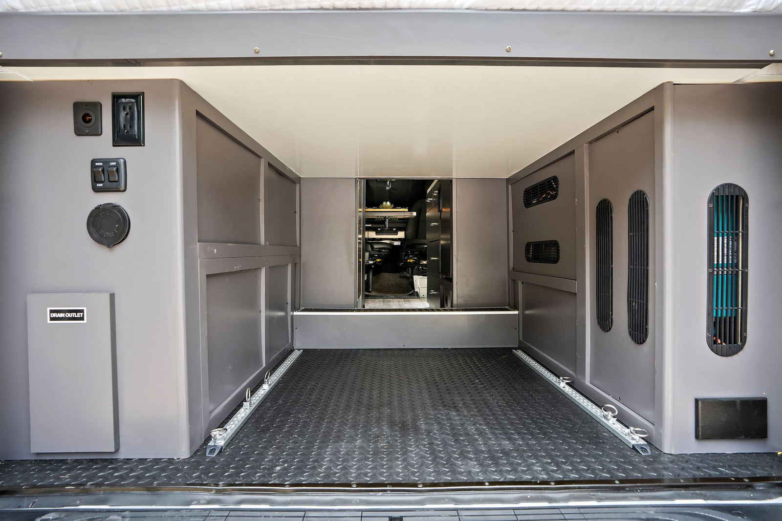 RV rental's rear utility area: power outlets, water/light controls, drain, vents, & floor tie-downs for secure cargo.