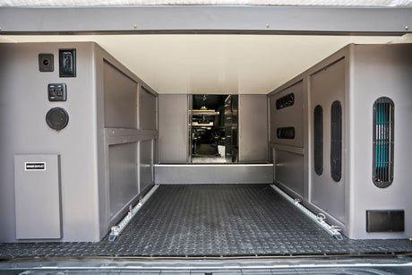 RV rental's rear utility area: power outlets, water/light controls, drain, vents, & floor tie-downs for secure cargo.