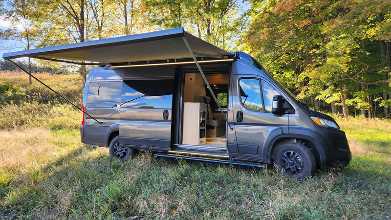 This grey camper van, perfect for RV rental, is parked in a sunny field with its awning extended and LED lights on. — photo 12