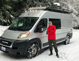 Man next to an RV rental van with tire chains, parked in a snowy forest. Ready for winter adventures!