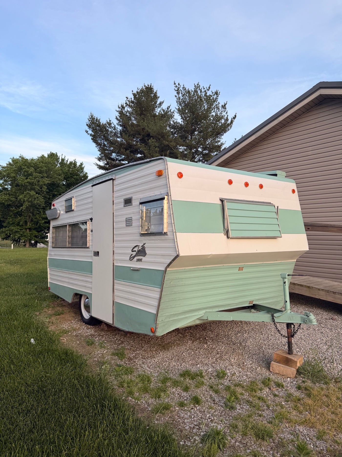 A classic two-tone Shasta camper, ideal for an RV rental, sits on gravel beside a grassy lawn, under a blue sky. — photo 7