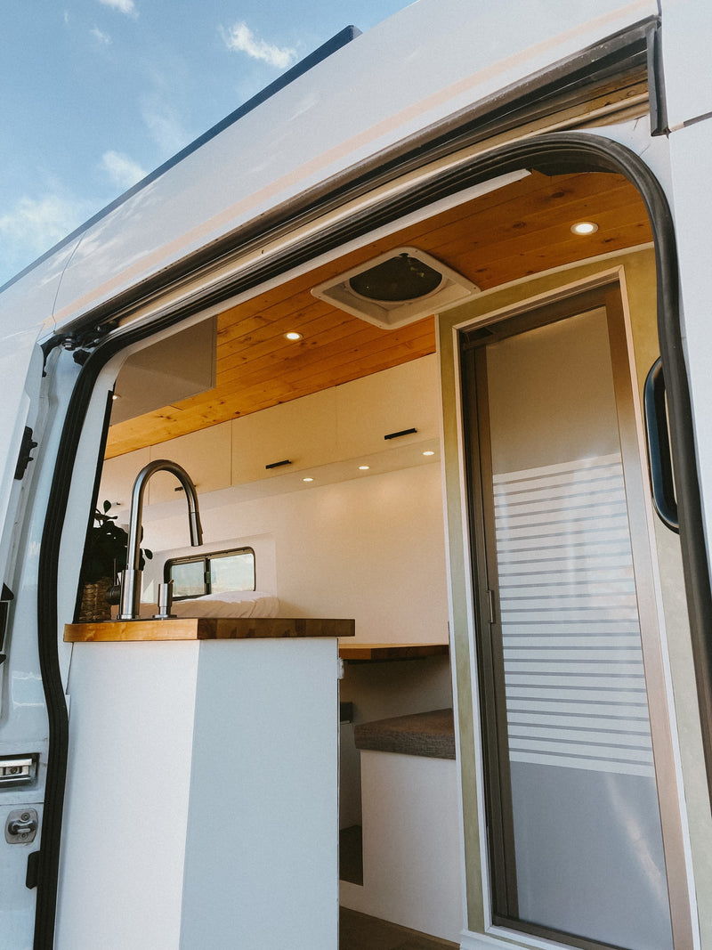 View inside a modern RV rental's bright interior: kitchen, wood ceilings, bed, and frosted sliding door. — photo 9