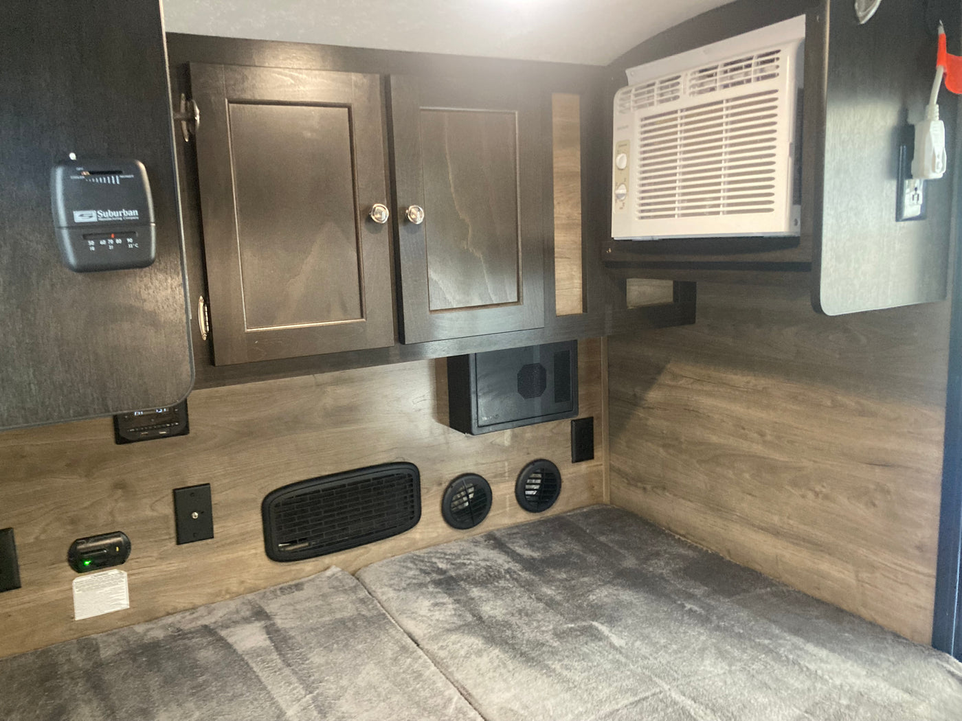 RV rental bedroom features a built-in AC unit, Suburban thermostat, overhead cabinets, and floor-level vents. — photo 4