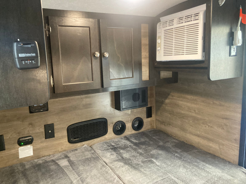 RV rental bedroom features a built-in AC unit, Suburban thermostat, overhead cabinets, and floor-level vents. — photo 4