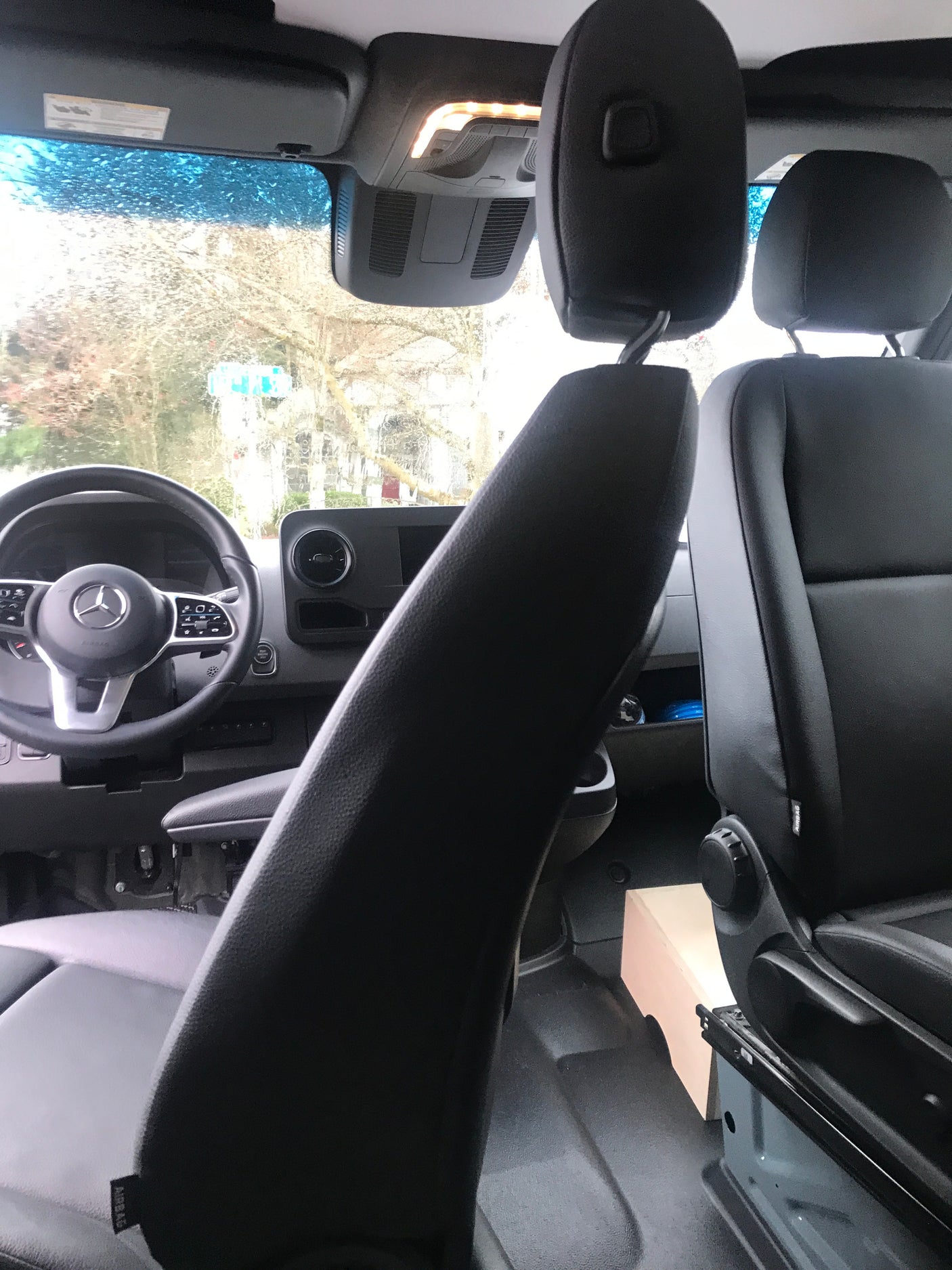 Interior of a Mercedes-Benz rv rental van, showcasing the dashboard, steering wheel, and passenger seats. Rain on windshield.