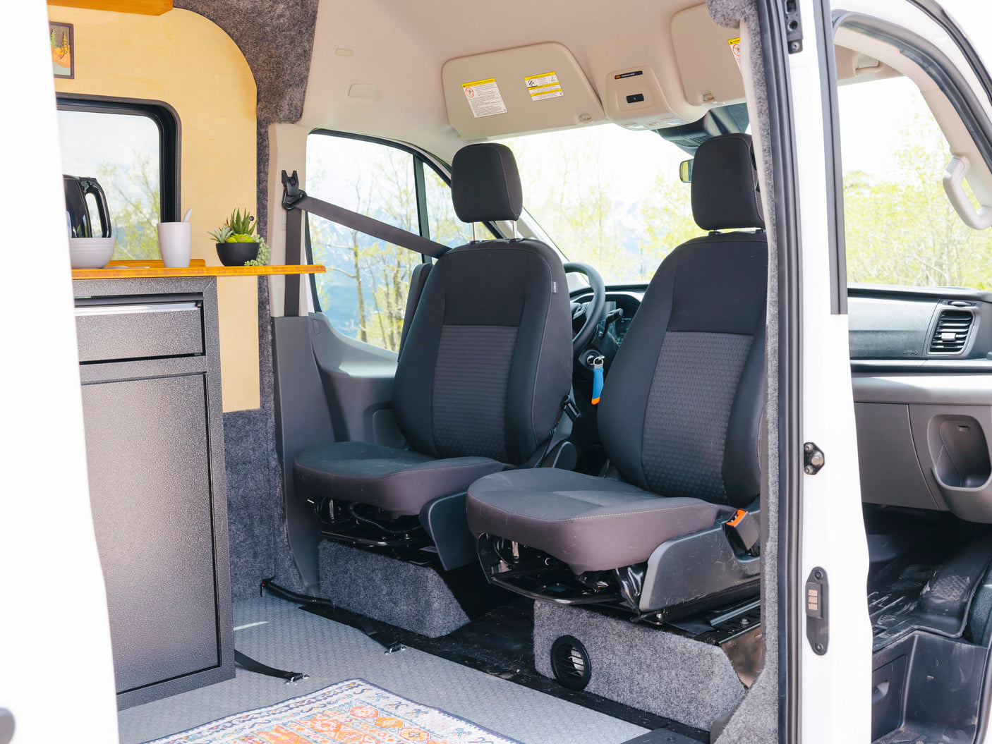 Interior of an RV rental camper van, showing kitchen area, front seats, and a custom build with amenities.
