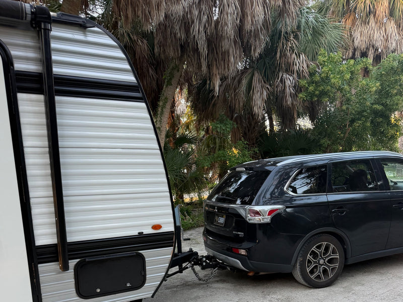  palm-filled campsite. A picnic table sits nearby on the gravel path.|A black SUV is hitched to a striped travel trailer RV rental — photo 6