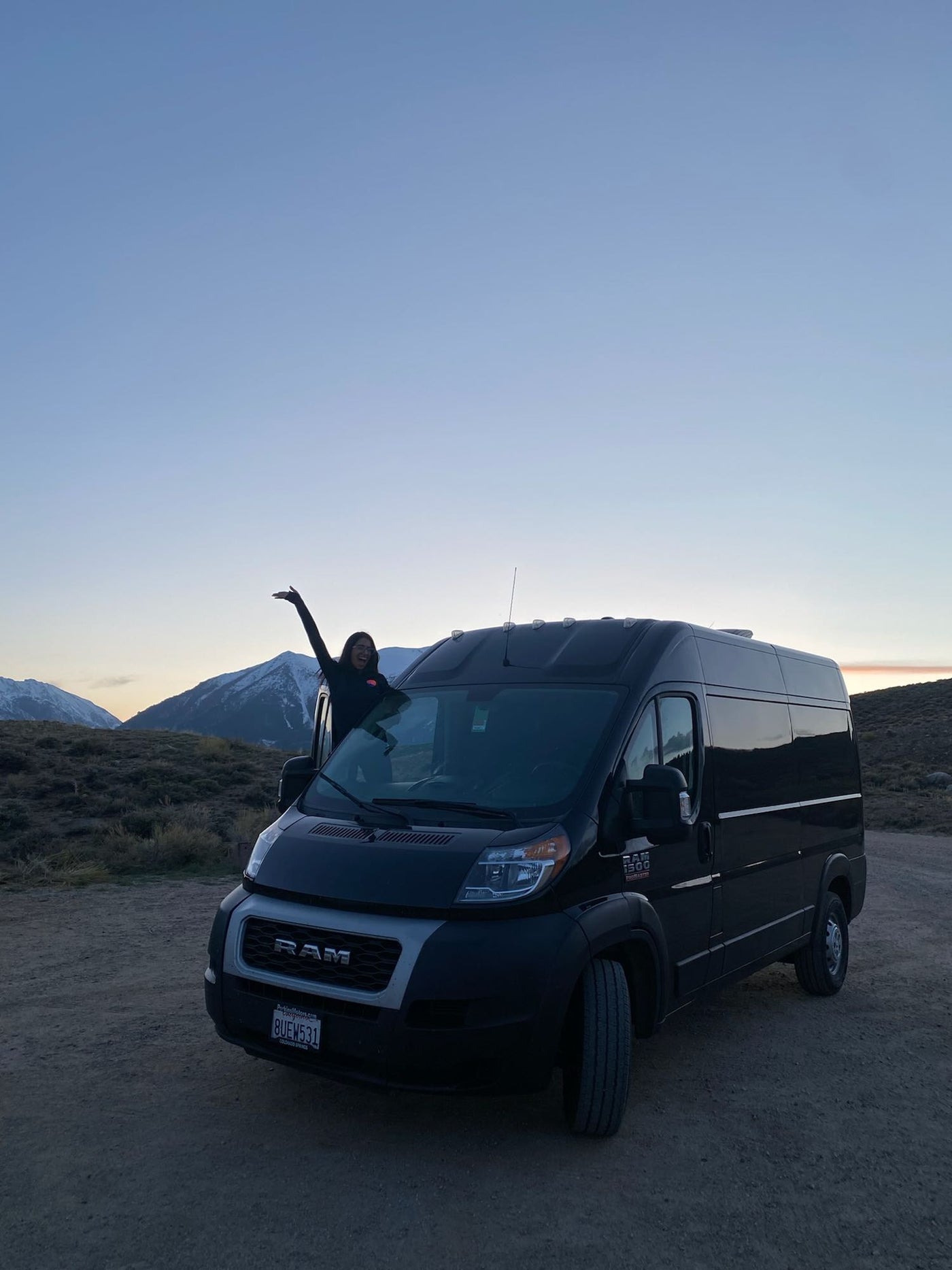  while a calico cat strolls on the dirt road.|Adventure-ready black Ram ProMaster RV rental parked on dirt — photo 8