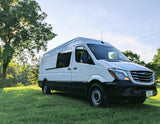 White Freightliner Sprinter camper van for RV rental, parked in a sunny grassy field, ready for adventure.