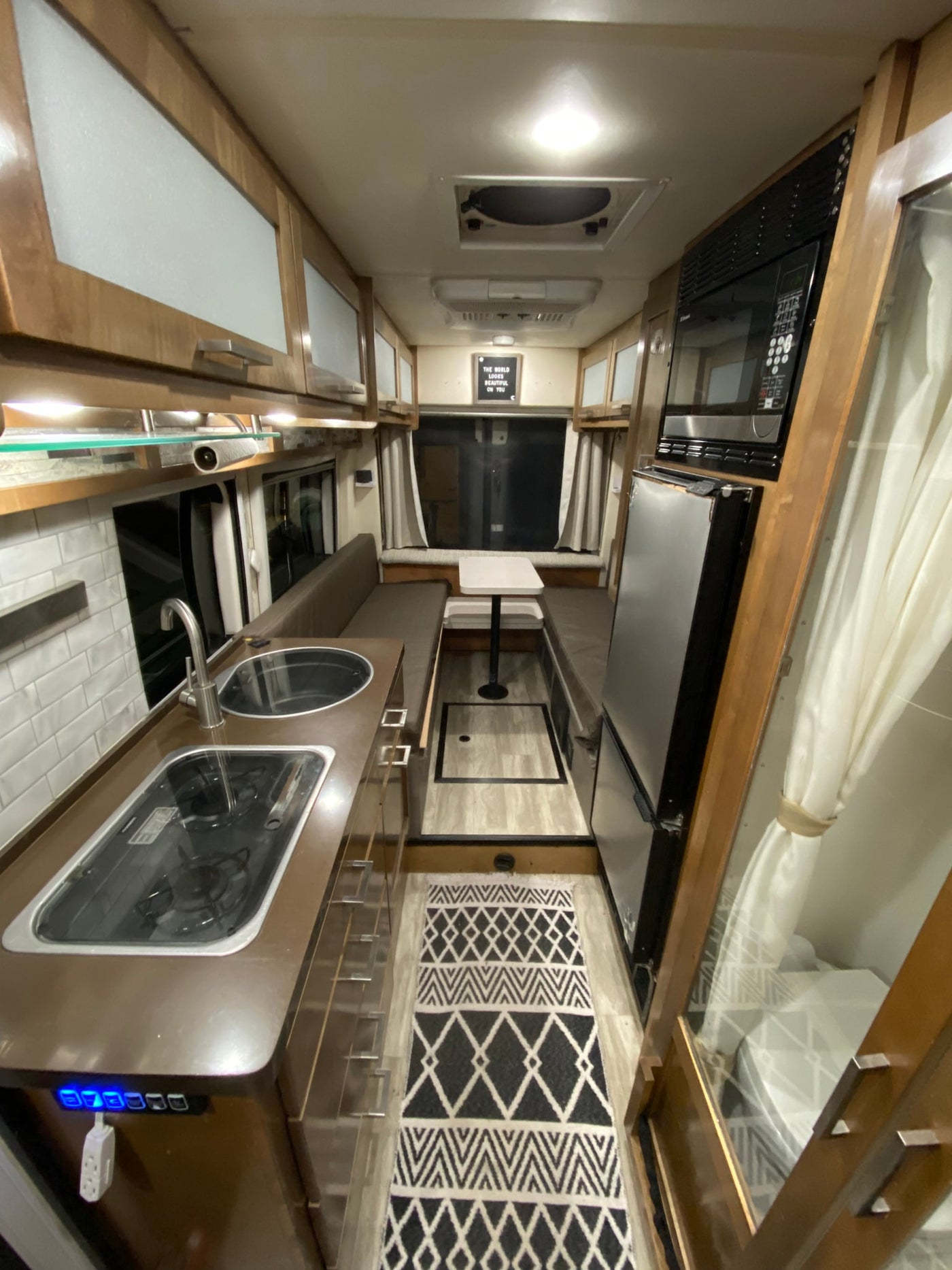 Step inside this RV rental showcasing a modern kitchen with stove, sink, microwave, fridge, and cozy dinette. — photo 7