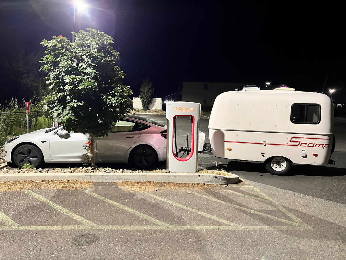 A white Tesla electric vehicle charges at night, hitched to a white Scamp RV rental, ready for camping adventures. — photo 18