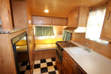 Interior of a retro RV rental: light wood paneling, compact kitchen, yellow dinette, and checkered floor.