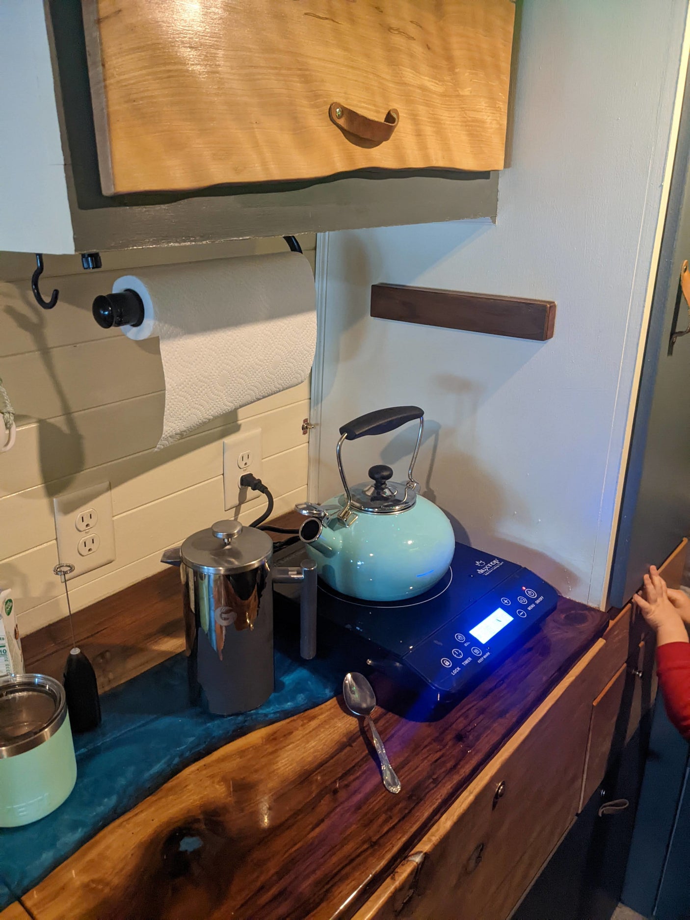 RV rental kitchen showing a light blue kettle on an induction cooktop, French press, and unique wood-and-resin counter.