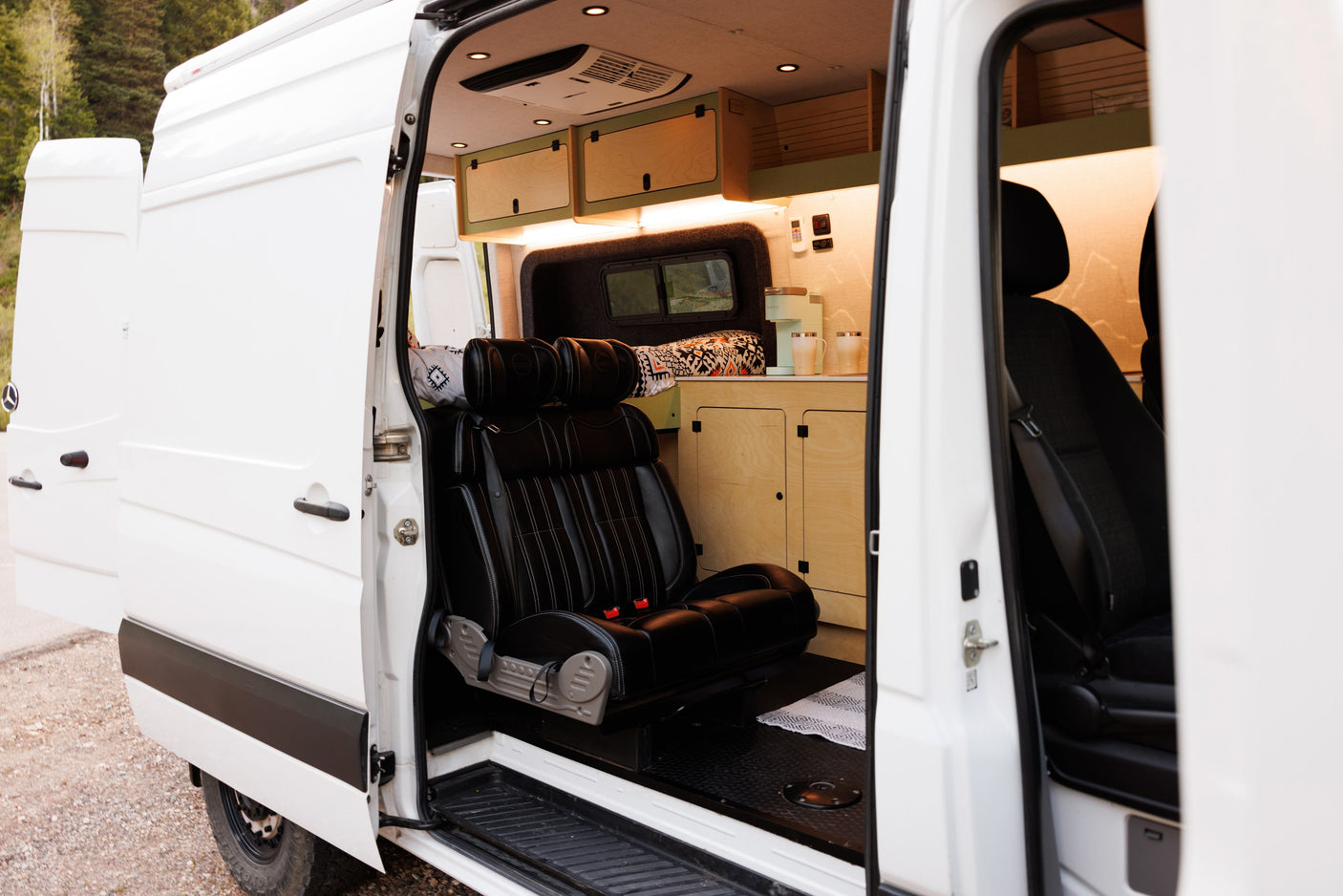 Open side doors reveal the inviting interior of an RV rental, featuring custom wood cabinets, comfortable seats, and a kitchen area.