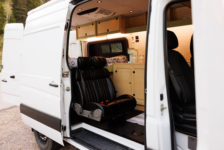 Open side doors reveal the inviting interior of an RV rental, featuring custom wood cabinets, comfortable seats, and a kitchen area.
