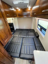 Inside this RV rental: a flexible black cushioned bed, overhead wood cabinets, and a window view. Ideal for compact living.