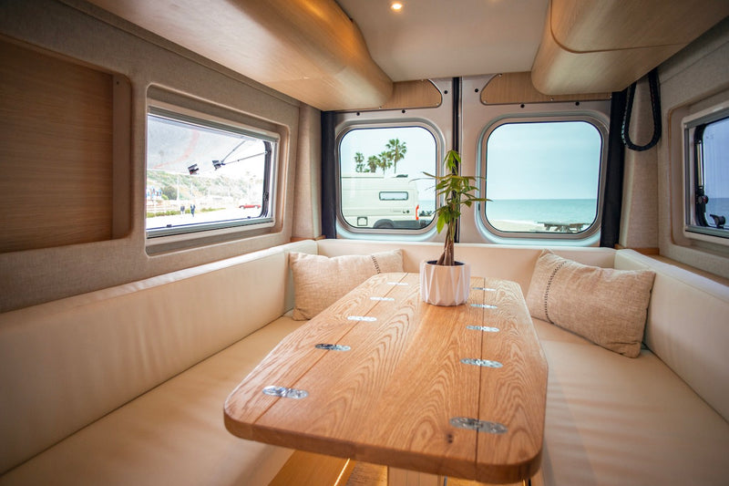 Experience comfort in this inviting RV rental interior, featuring a custom wooden table, plush seating, and scenic beach views. — photo 19