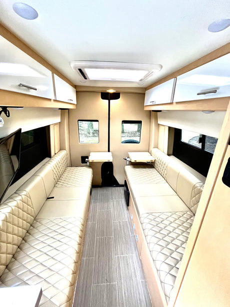 Clean, modern RV rental interior featuring plush, quilted bench seating, wood-look floor, and bright lighting.
